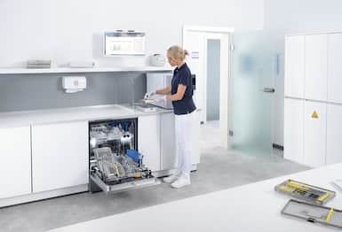 Modern sterile clinic reprocessing room; gloved staff handles instrument trays by an open washer-disinfector.