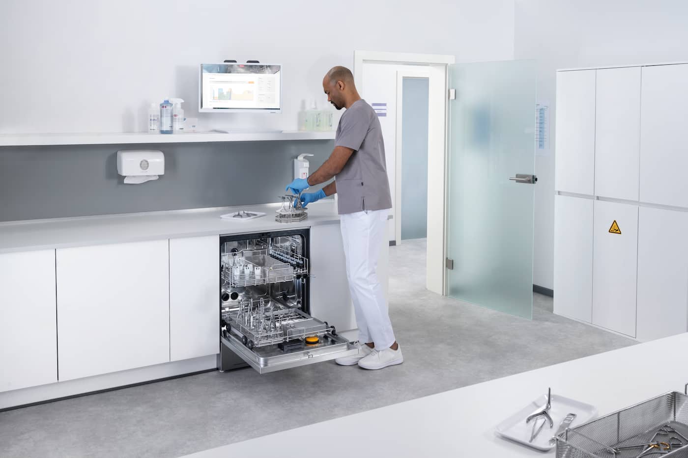 Clinician in a sterile reprocessing room loading medical instruments into a washer-disinfector.
