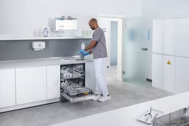 Clinician in a sterile reprocessing room loading medical instruments into a washer-disinfector.