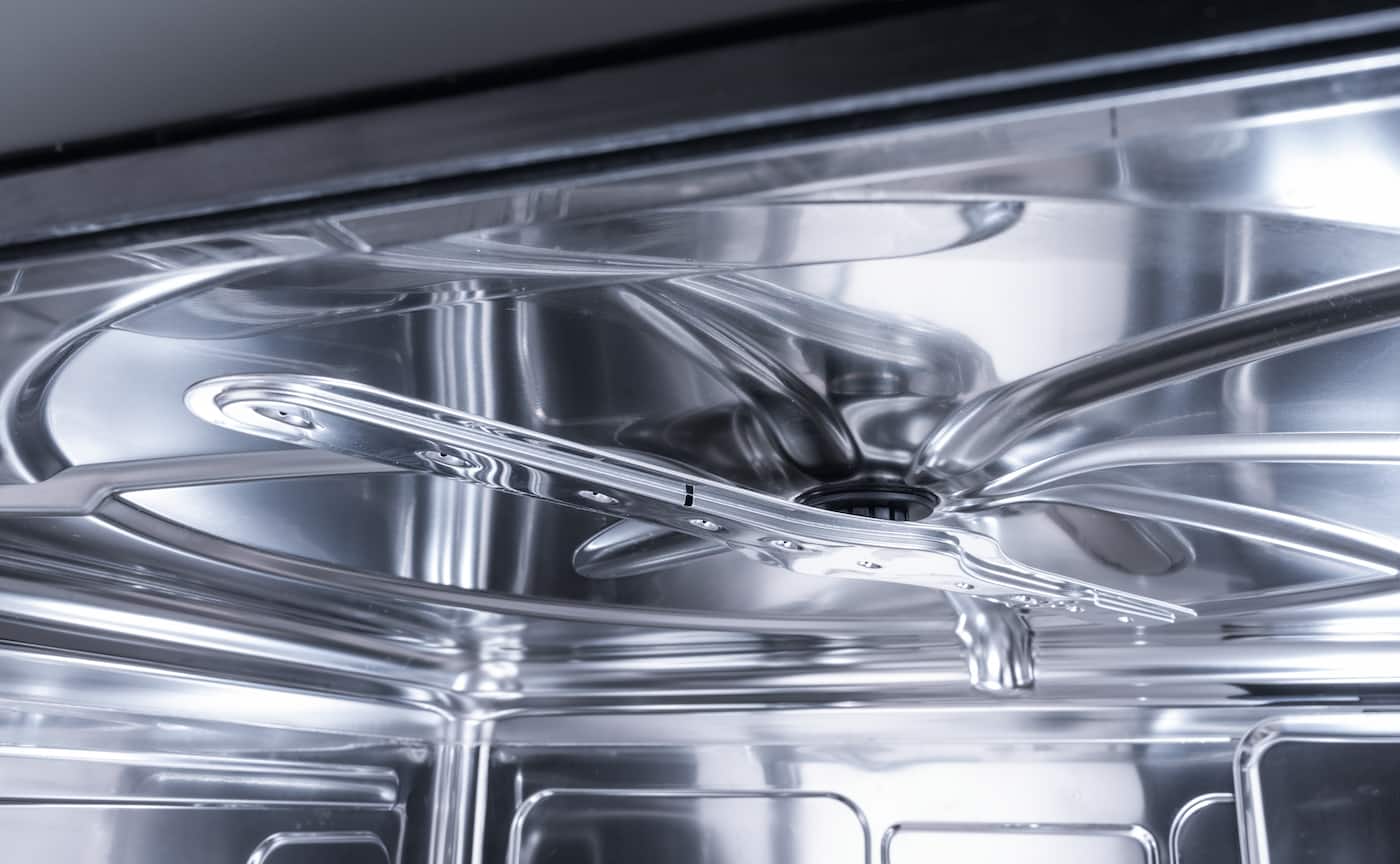 Close-up of a stainless steel dishwasher interior showing the rotating spray arm and reflective tub.
