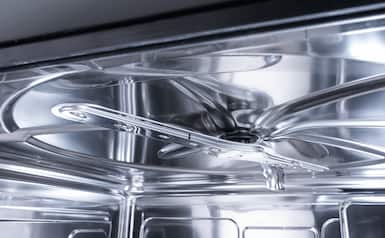 Close-up of a stainless steel dishwasher interior showing the rotating spray arm and reflective tub.